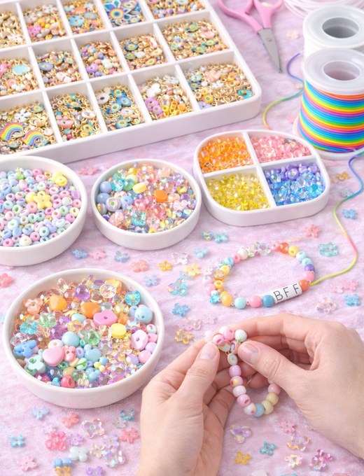 Girls sitting together making charm bracelets at a sleepover, focused and smiling