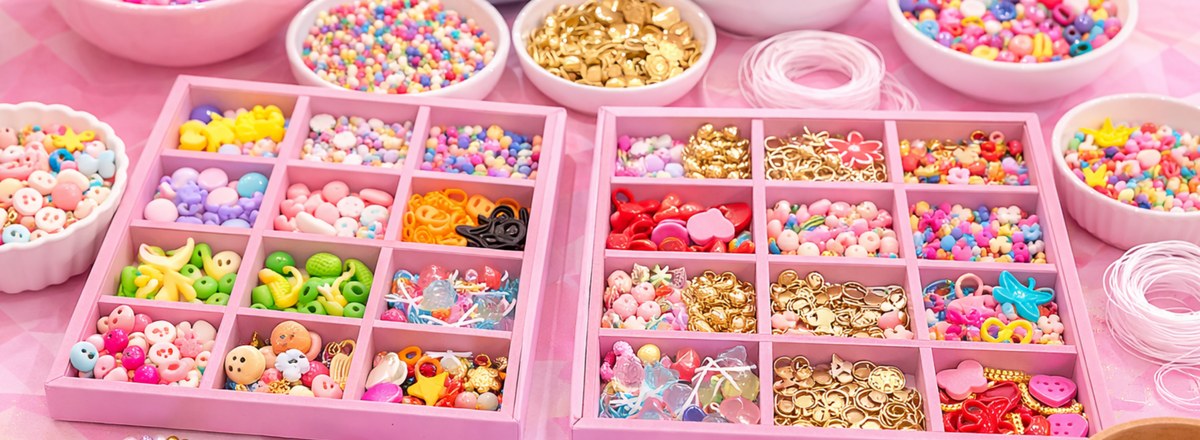 A beautifully arranged charm bracelet making station with colorful beads, charms, and string on a soft pastel tablecloth