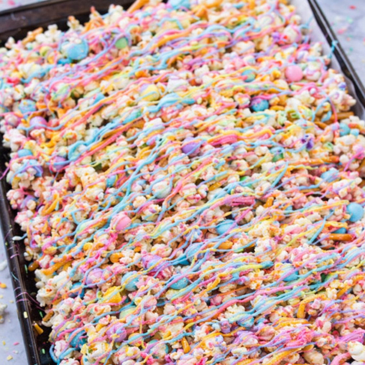Finished Unicorn Popcorn Snack Mix in a bowl, covered in pastel chocolate drizzle and rainbow sprinkles